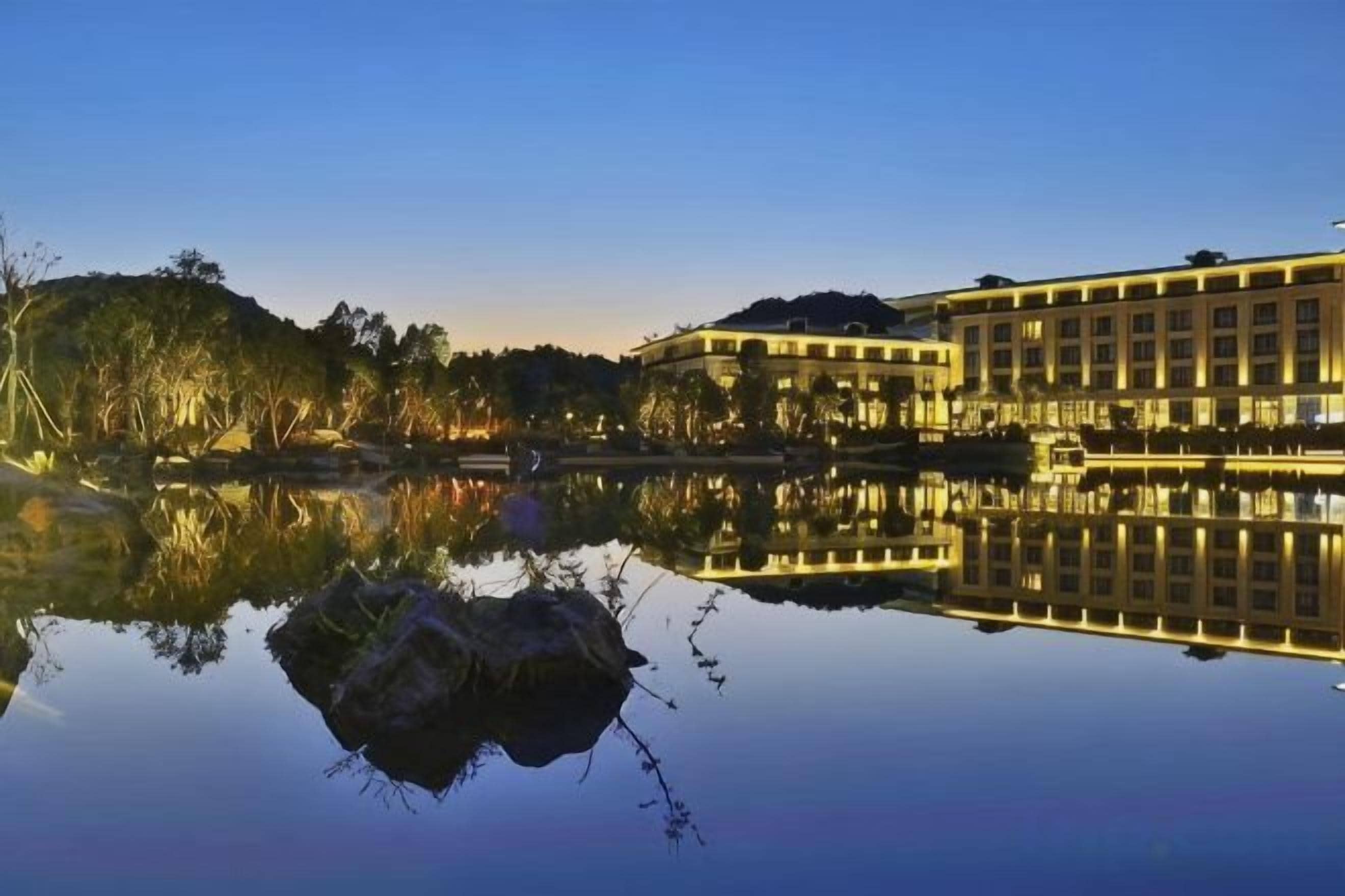 A building with a reflection in a calm body of water, surrounded by trees and a clear sky.