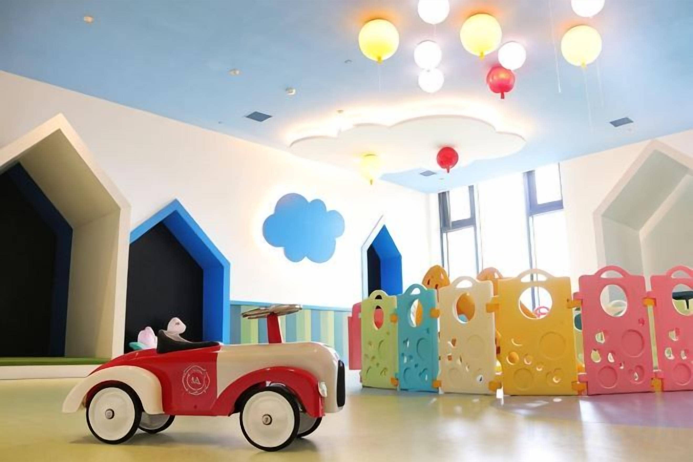 A children's play area with a toy car, colorful play structures, and a ceiling with decorative lights.