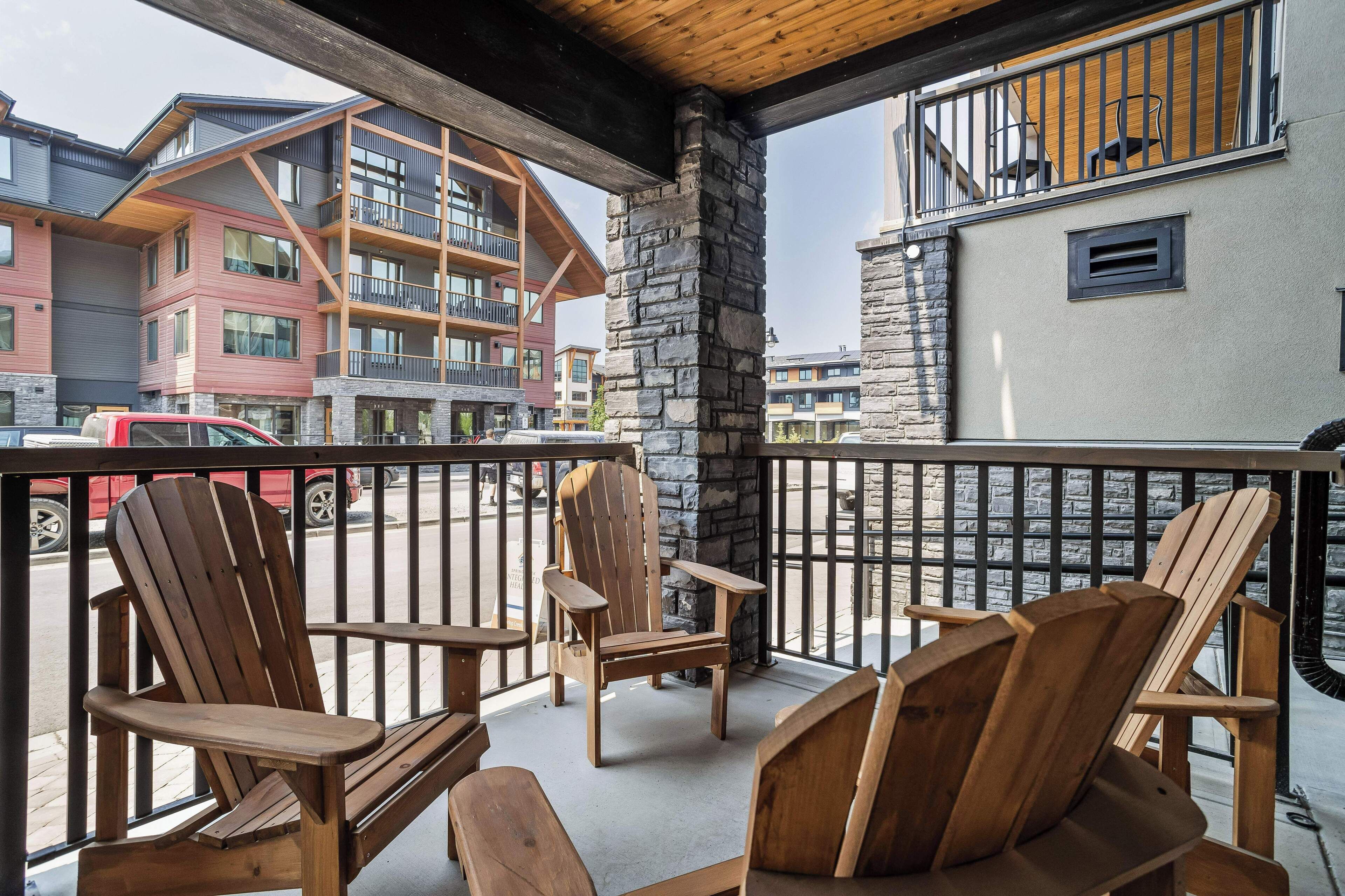 A balcony with wooden Adirondack chairs, a stone pillar, and a view of multi-story buildings.