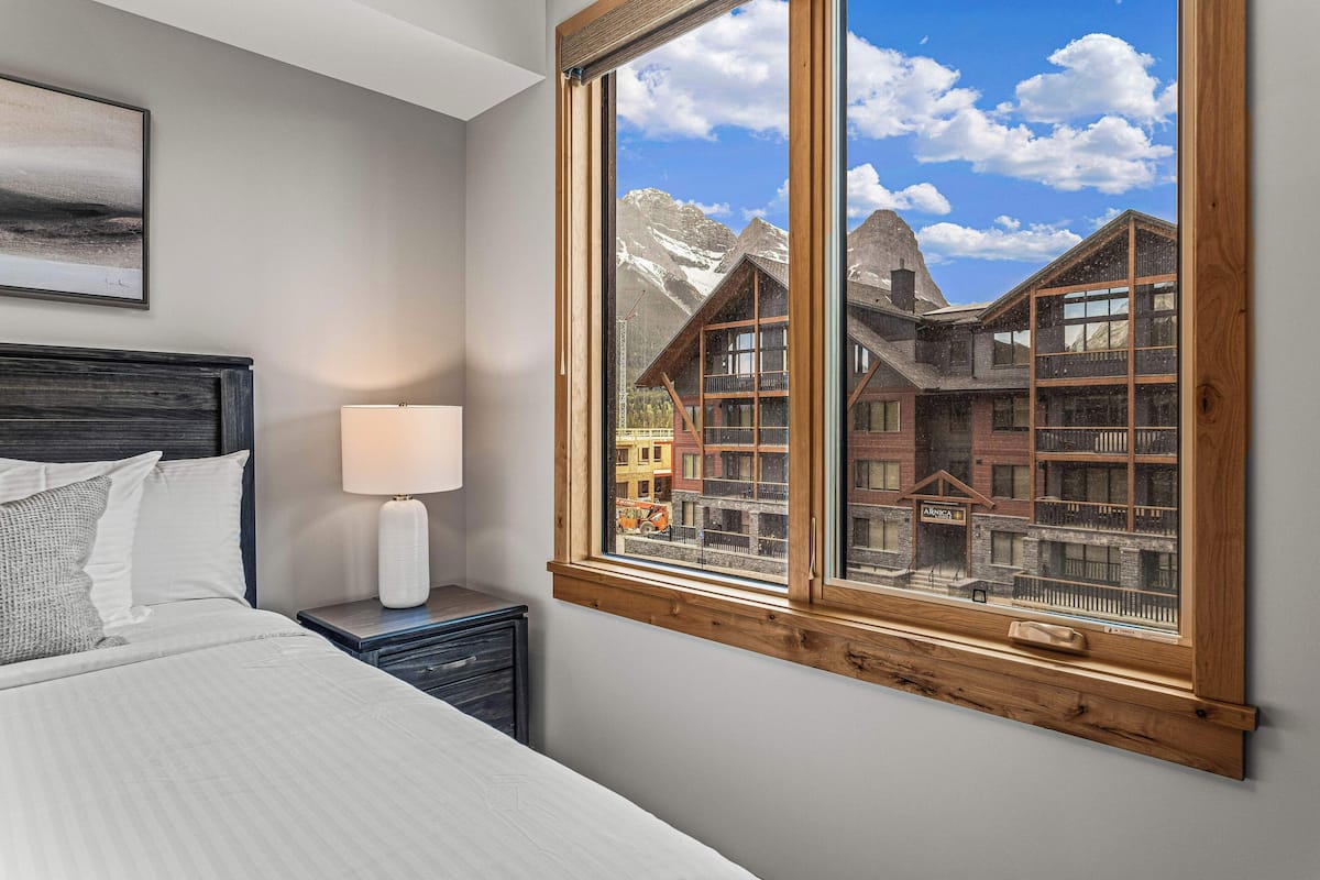 A bedroom with a large window, a bed, a nightstand, and a lamp.