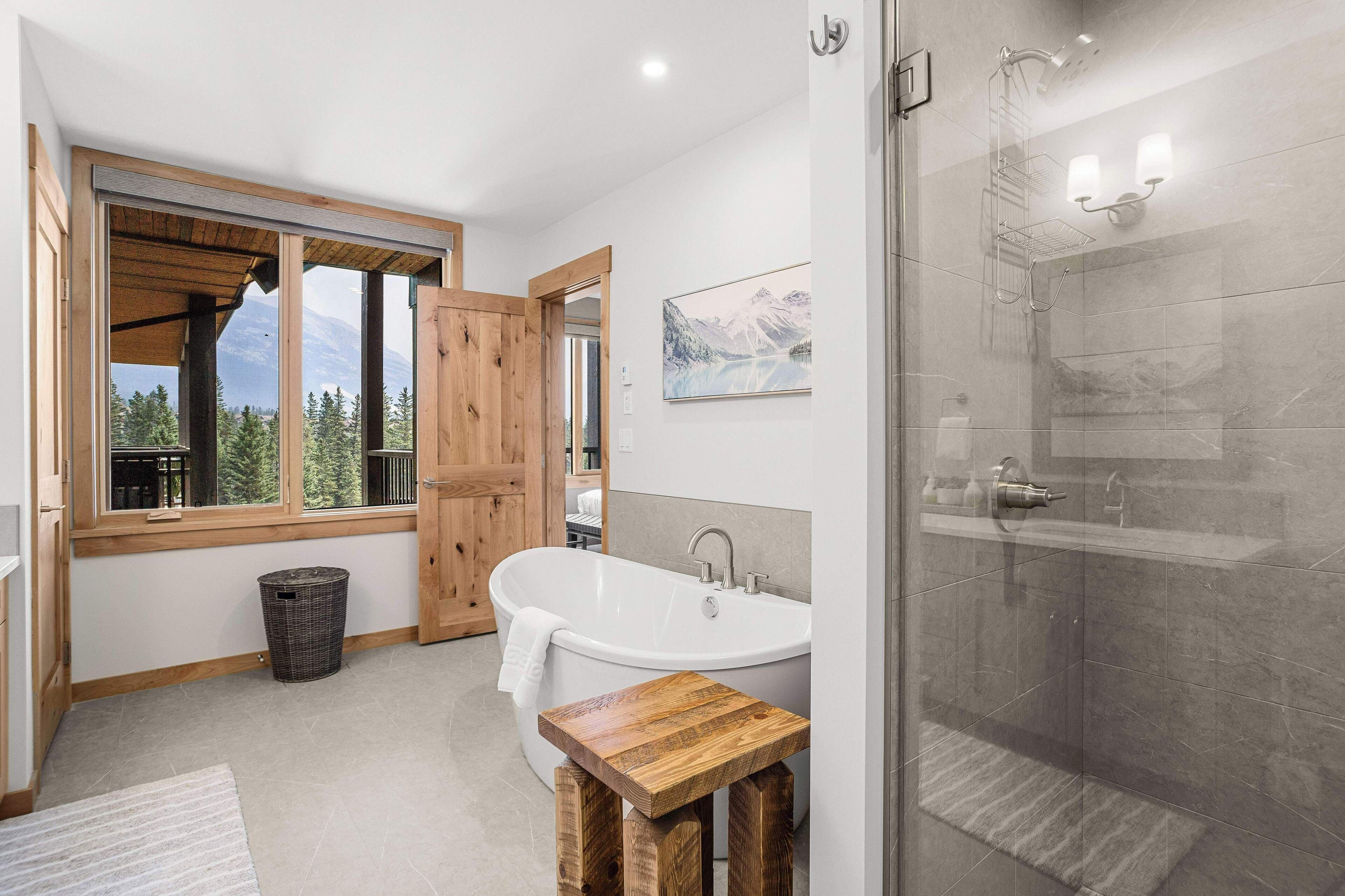 Une salle de bain moderne dotée d’une baignoire sur pieds, d’une douche à parois de verre et d’une grande fenêtre offrant une vue sur les montagnes.