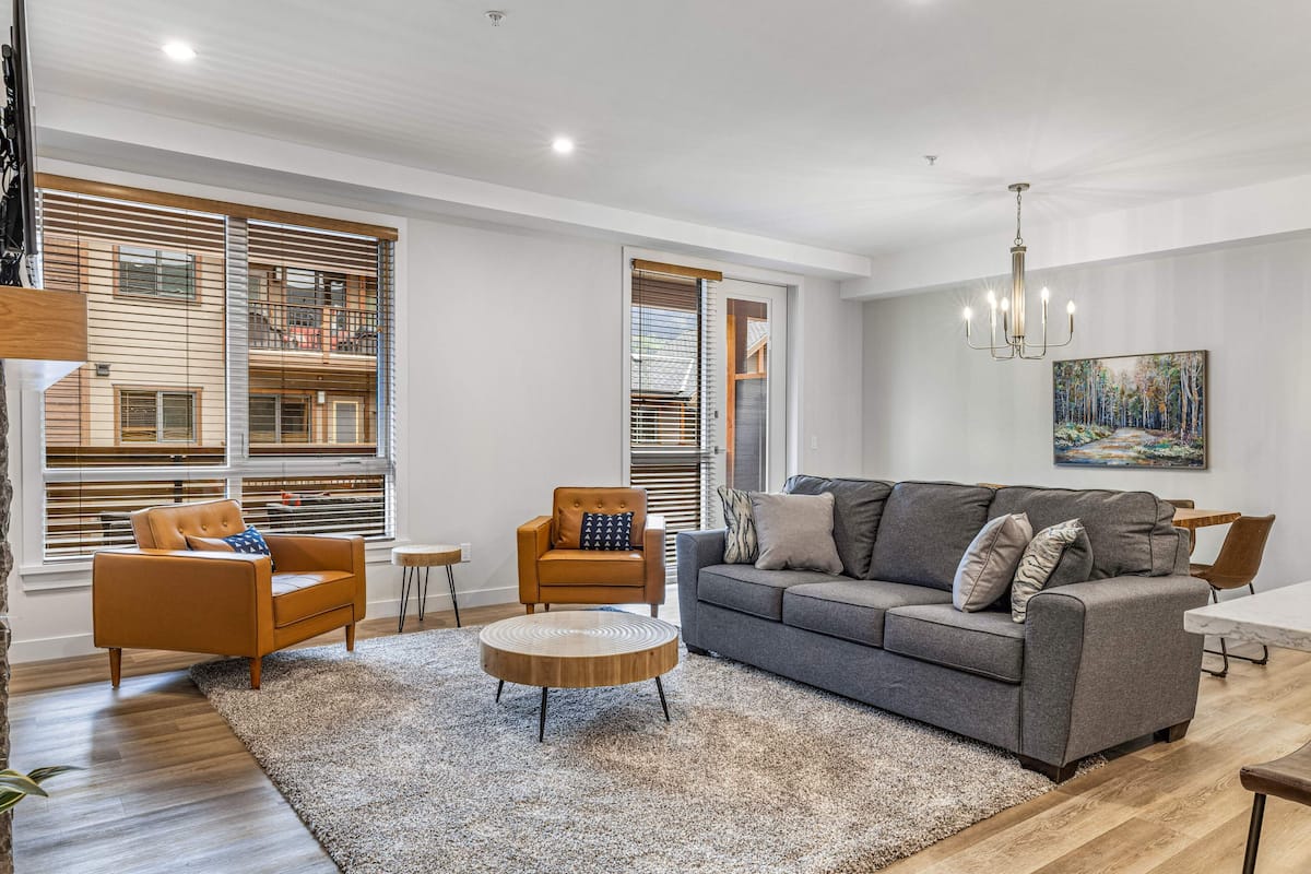 Una sala de estar moderna con un sofá gris, un sillón marrón y una mesa de centro redonda.