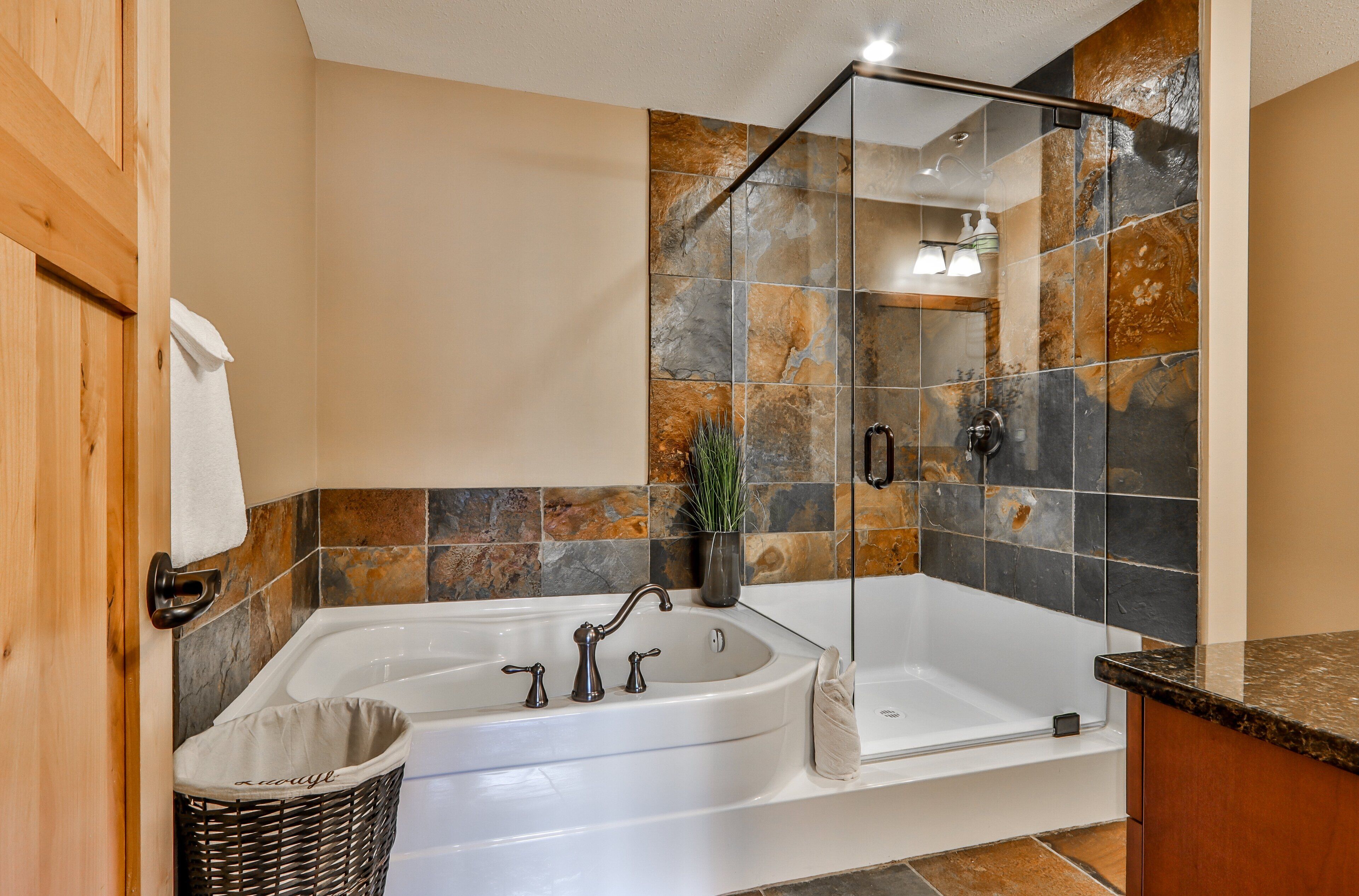 A modern bathroom with a large bathtub, a glass shower enclosure, and a wooden door.