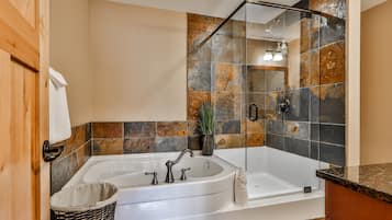 A modern bathroom with a large bathtub, a glass shower enclosure, and a wooden door.