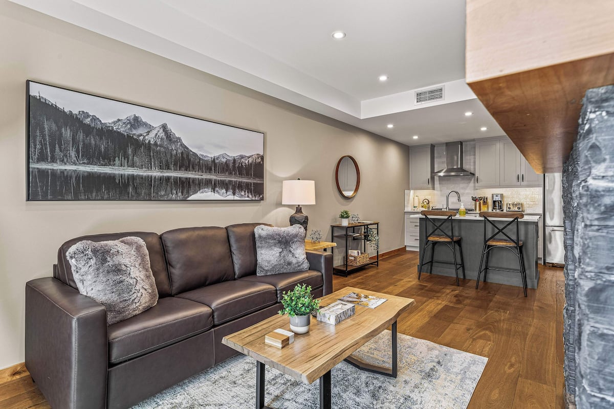 A modern living room with a brown leather sofa, a wooden coffee table, and a large landscape painting.