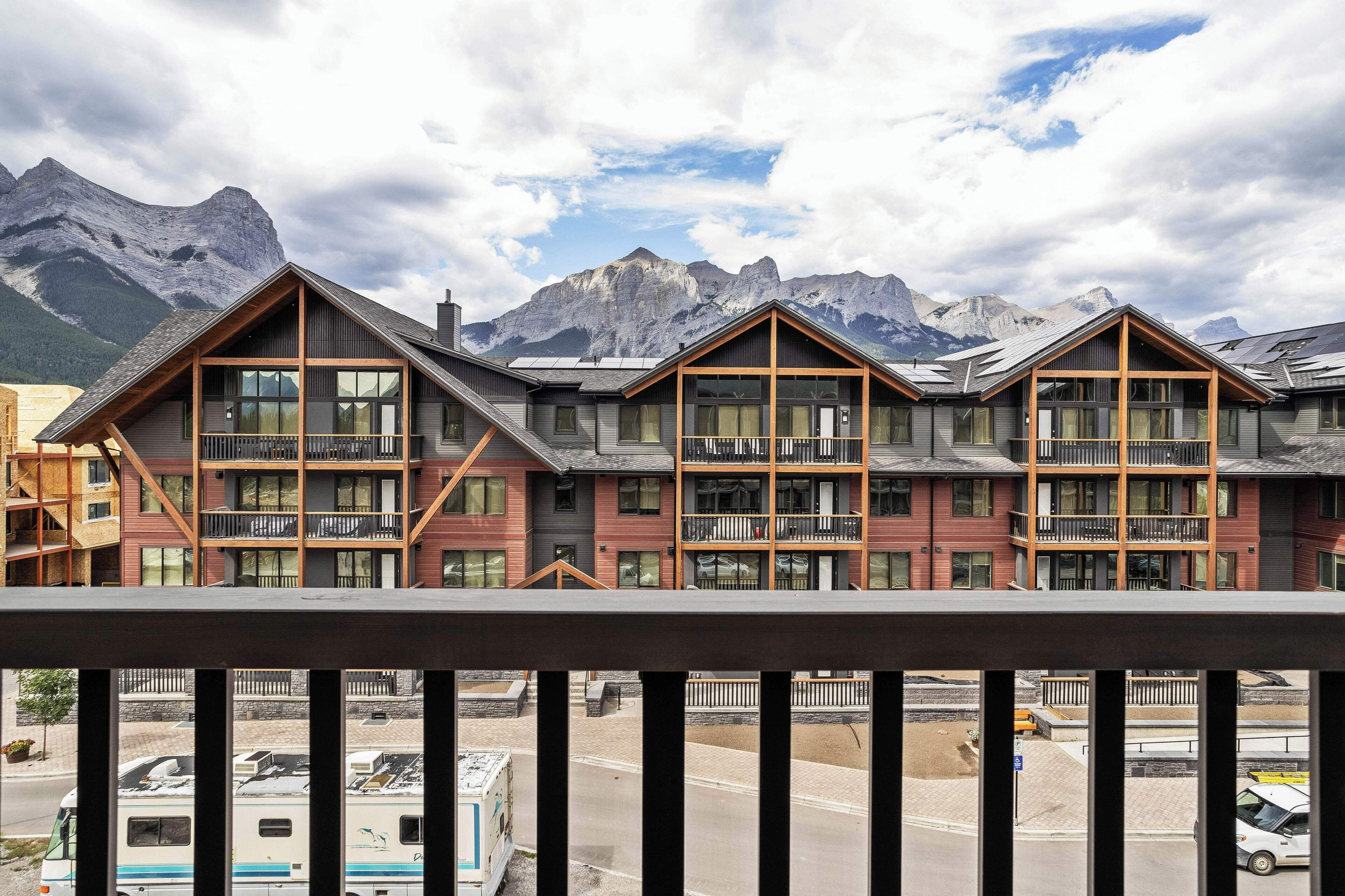 A modern hotel with multiple balconies and large windows, set against a backdrop of mountains.
