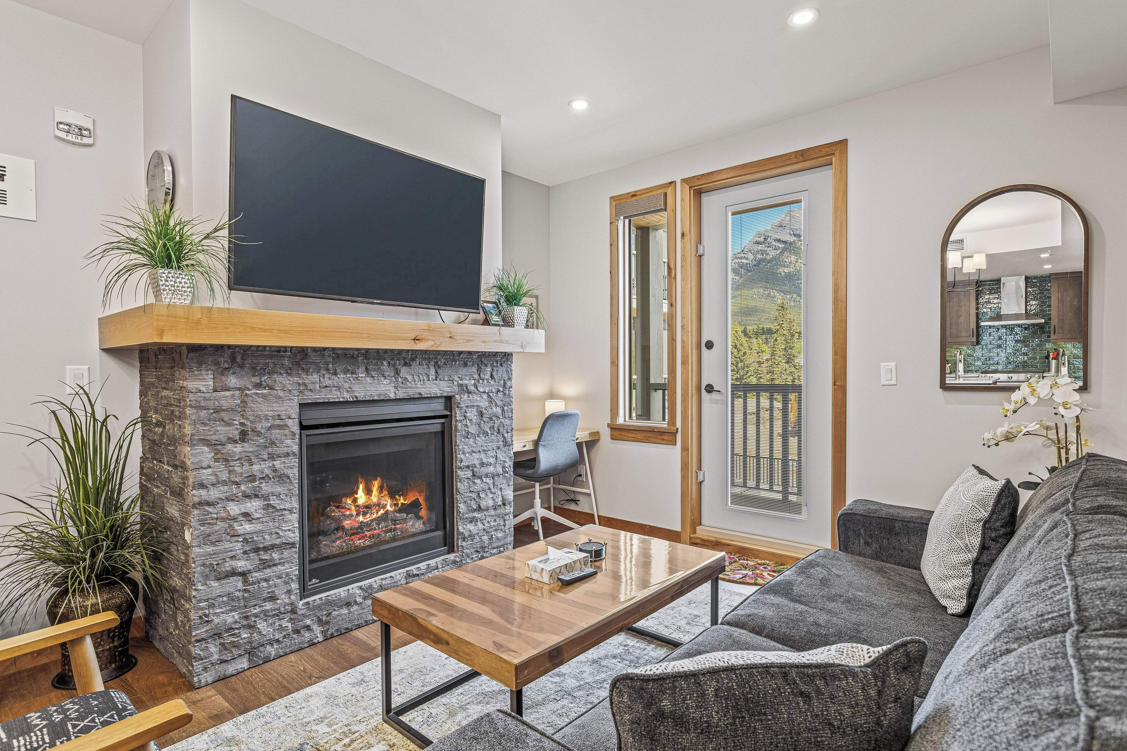 A modern living room with a stone fireplace, a flat-screen TV, a comfortable sofa, and a dining area.