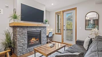 A modern living room with a stone fireplace, a flat-screen TV, a comfortable sofa, and a dining area.