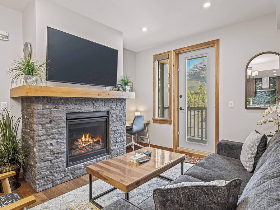 A modern living room with a stone fireplace, a flat-screen TV, a comfortable sofa, and a dining area.