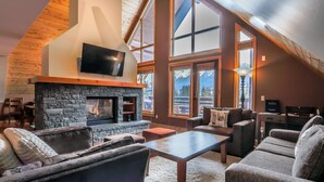 A cozy living room with a stone fireplace, comfortable seating, and large windows offering mountain views.