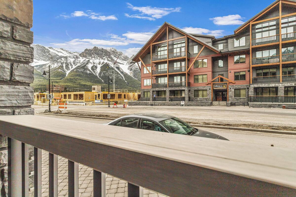 A multi-story building with a stone facade and balconies, set against a mountainous backdrop.