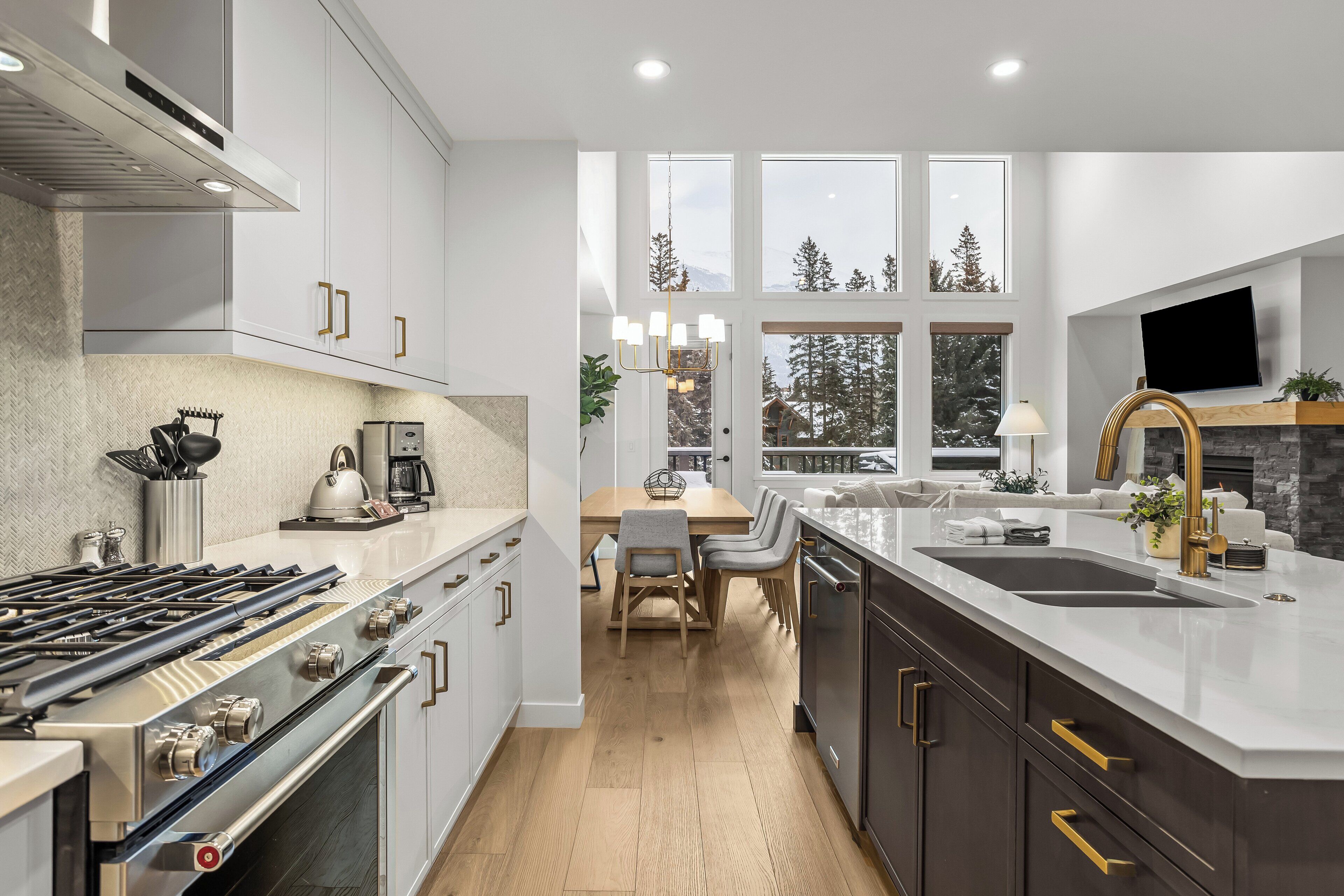 Una cocina moderna con una isla central, electrodomésticos de acero inoxidable y grandes ventanales con vista a árboles.