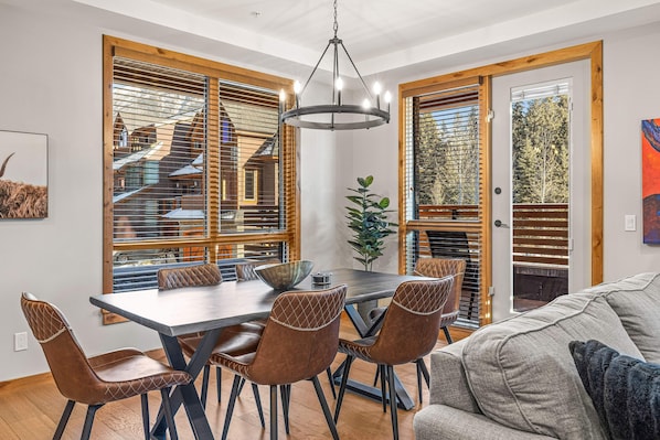 Un espace repas comprenant une grande table et des chaises, des stores en bois et un lustre.