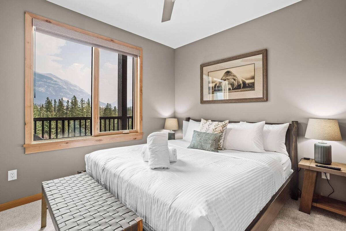 A bedroom with a large bed, a bench, a nightstand, a lamp, and a framed picture on the wall.