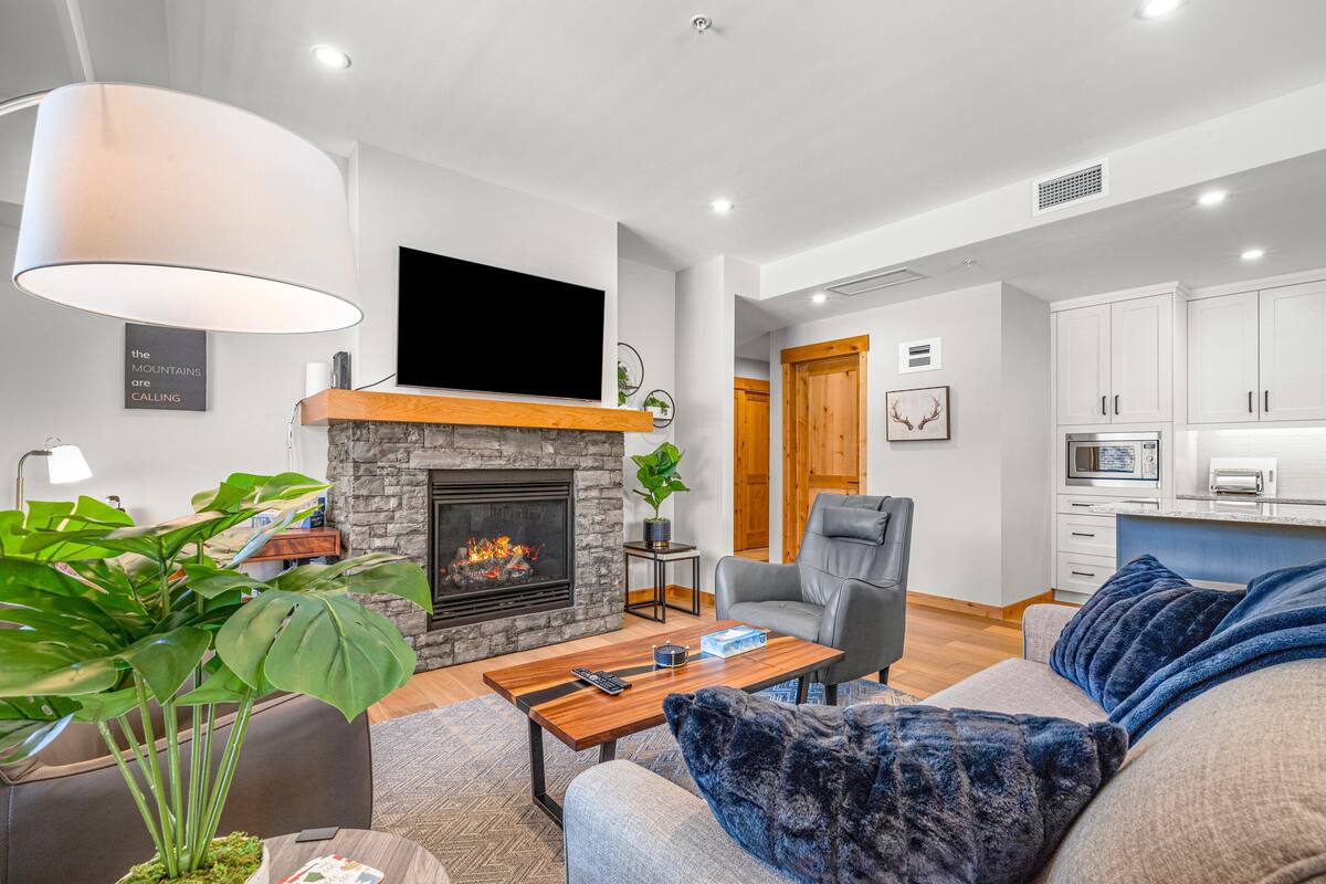Una sala moderna con chimenea, televisor de pantalla plana, sofá c ómodo y comedor con cocina al fondo.