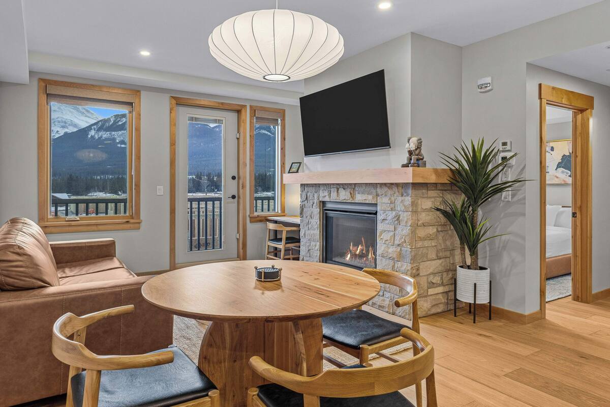A cozy living room with a fireplace, wooden furniture, and large windows offering mountain views.