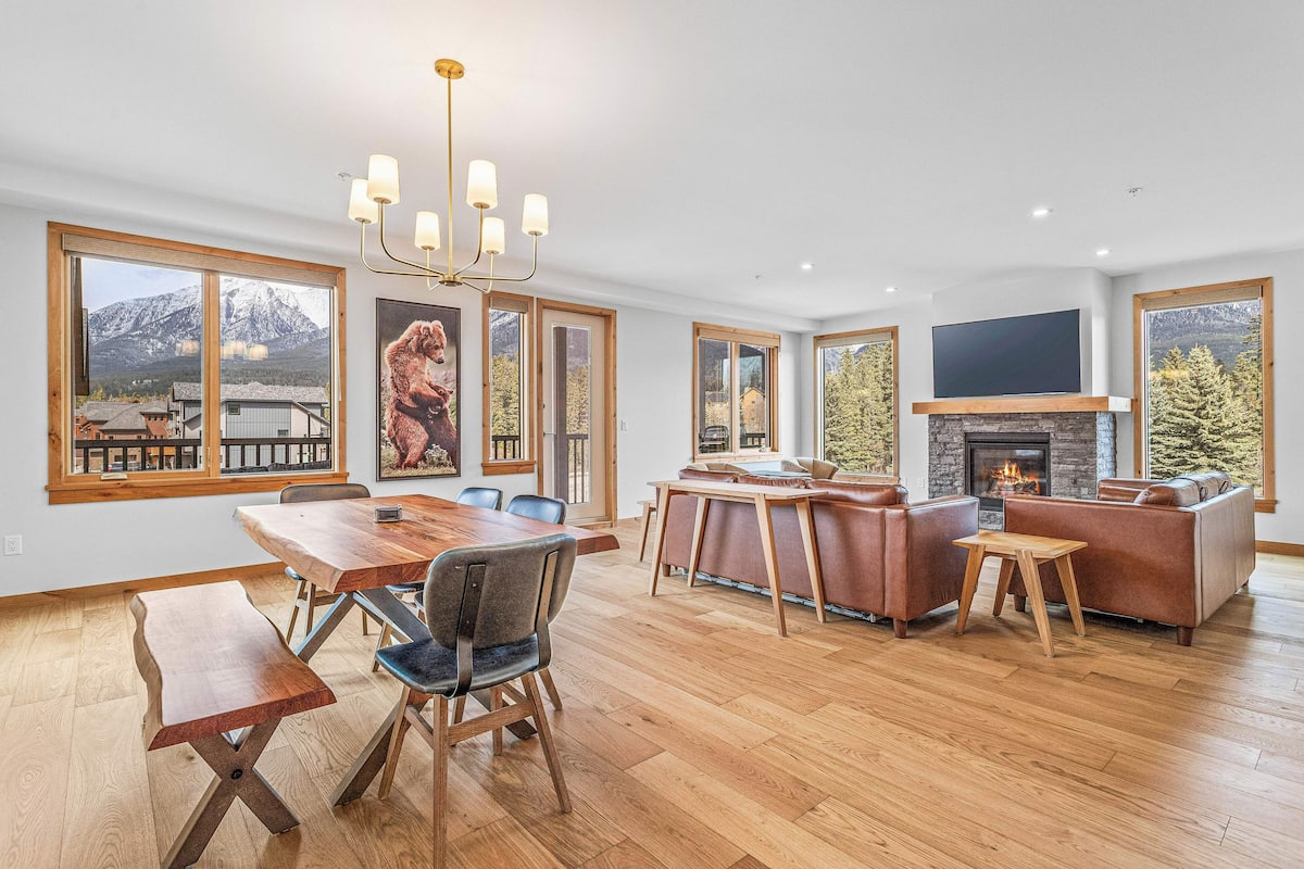 A spacious living area with a fireplace, large windows, and a dining table.