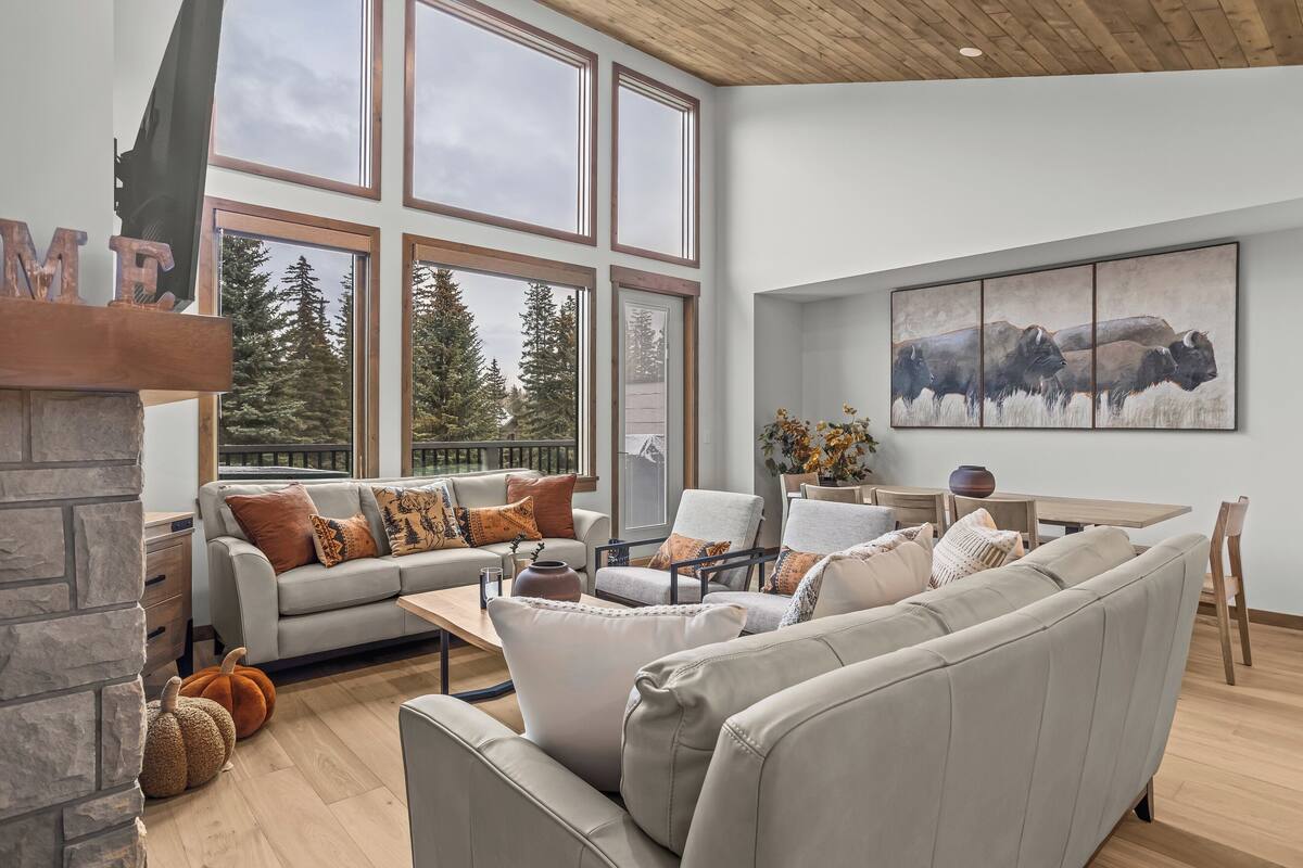 A modern living room with a fireplace, large windows, and a painting of bison.
