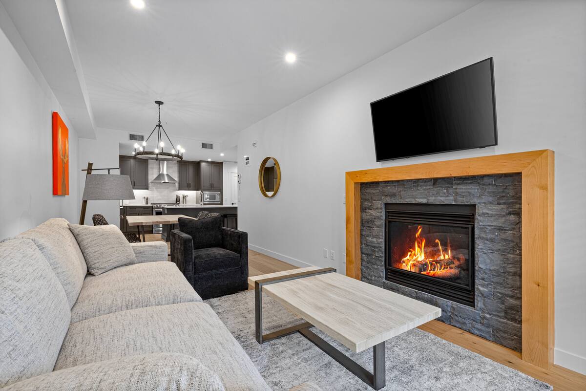 Una sala de estar moderna con chimenea, un sofá, una mesa de centro y un televisor montado en la pared.