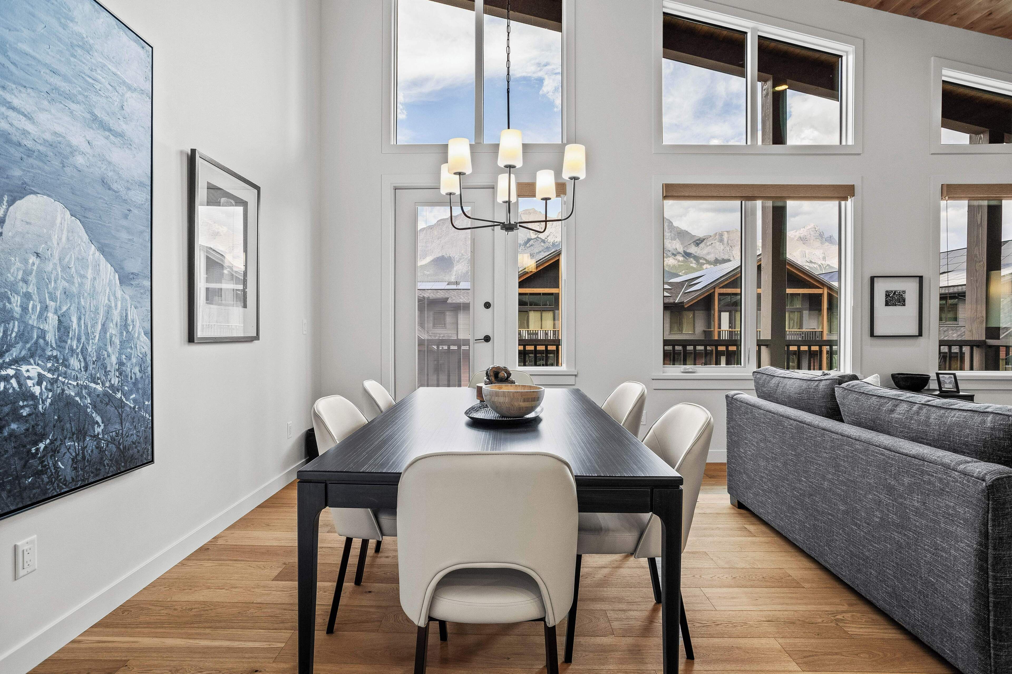 Uma sala de jantar moderna com uma mesa comprida, cadeiras brancas e um candelabro.
