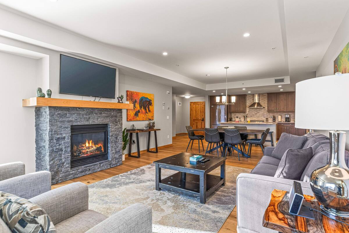 Una sala de estar moderna con chimenea, sofás grises, una mesa de centro y un televisor montado en la pared.