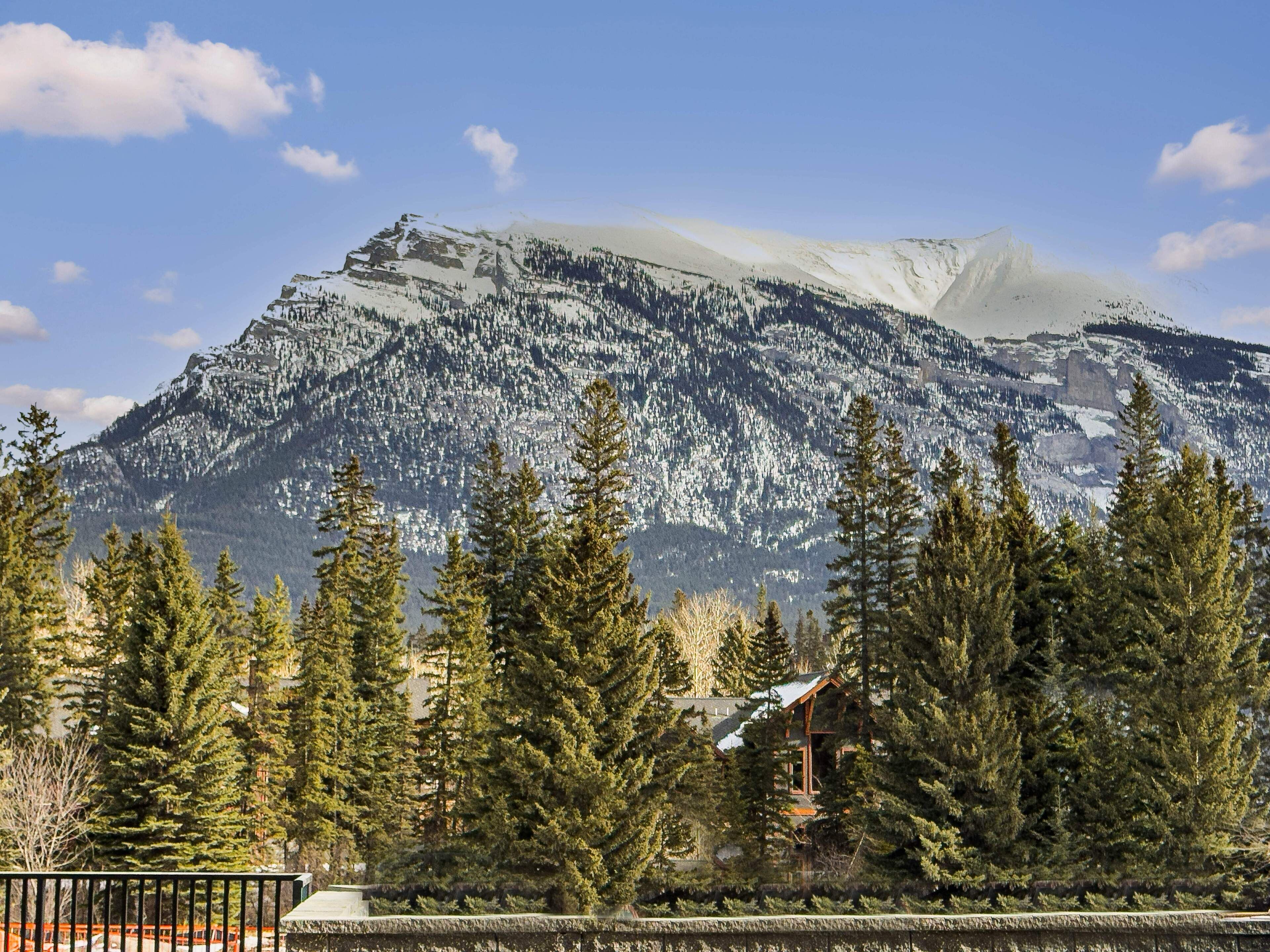 A mountain with snow-covered peaks and a cabin in the foreground.