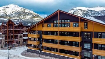 Un hotel moderno con varios balcones y ventanas amplias, con vistas a montañas nevadas.