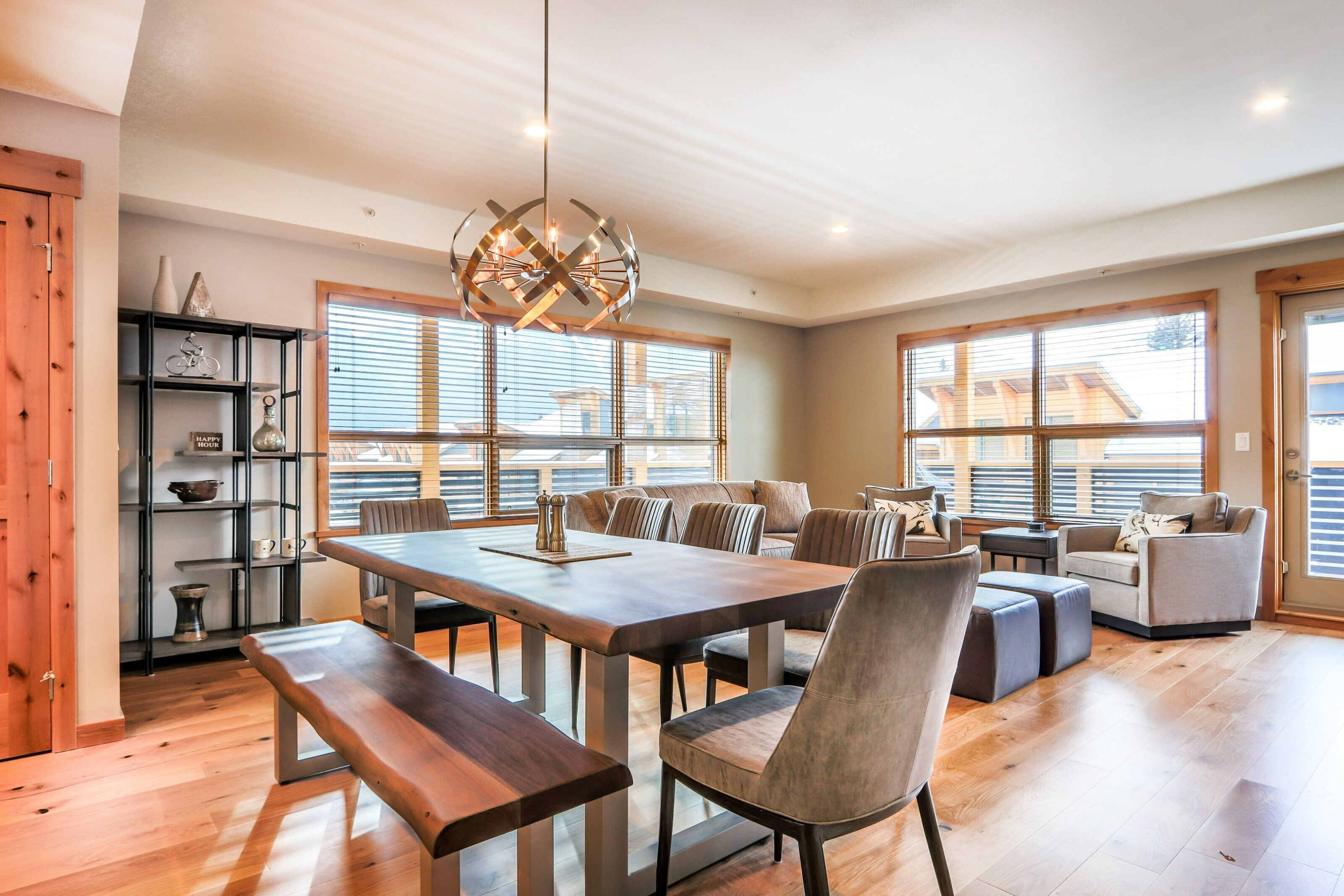 Een ruime woonkamer met een houten eettafel, zithoek en grote ramen voor natuurlijk licht.
