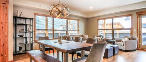 A spacious living area with a wooden dining table, comfortable seating, and large windows providing natural light.