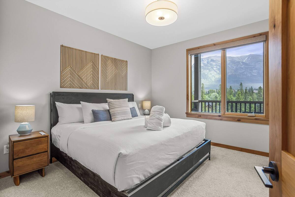 A bedroom with a large bed, a nightstand, a window with a mountain view, and decorative wall panels.