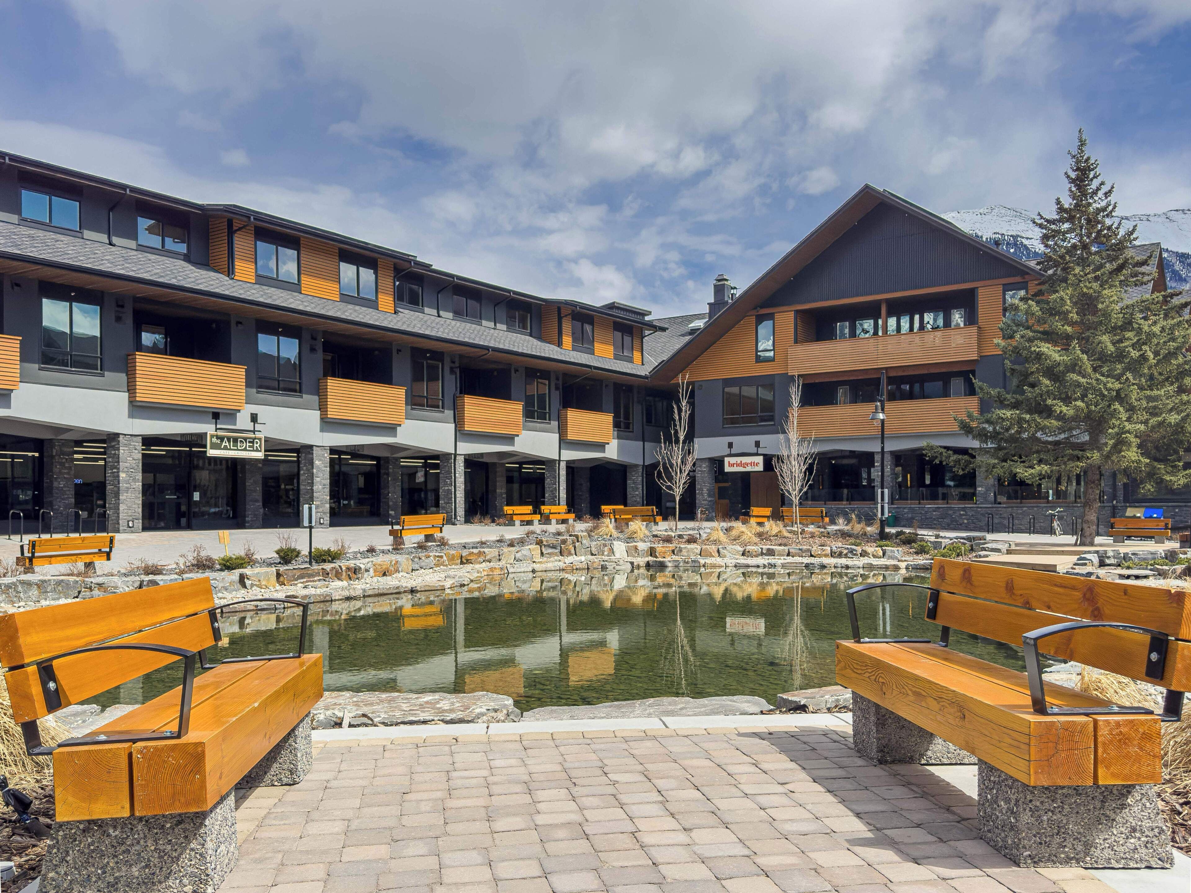 A modern hotel with outdoor seating and a central pond.