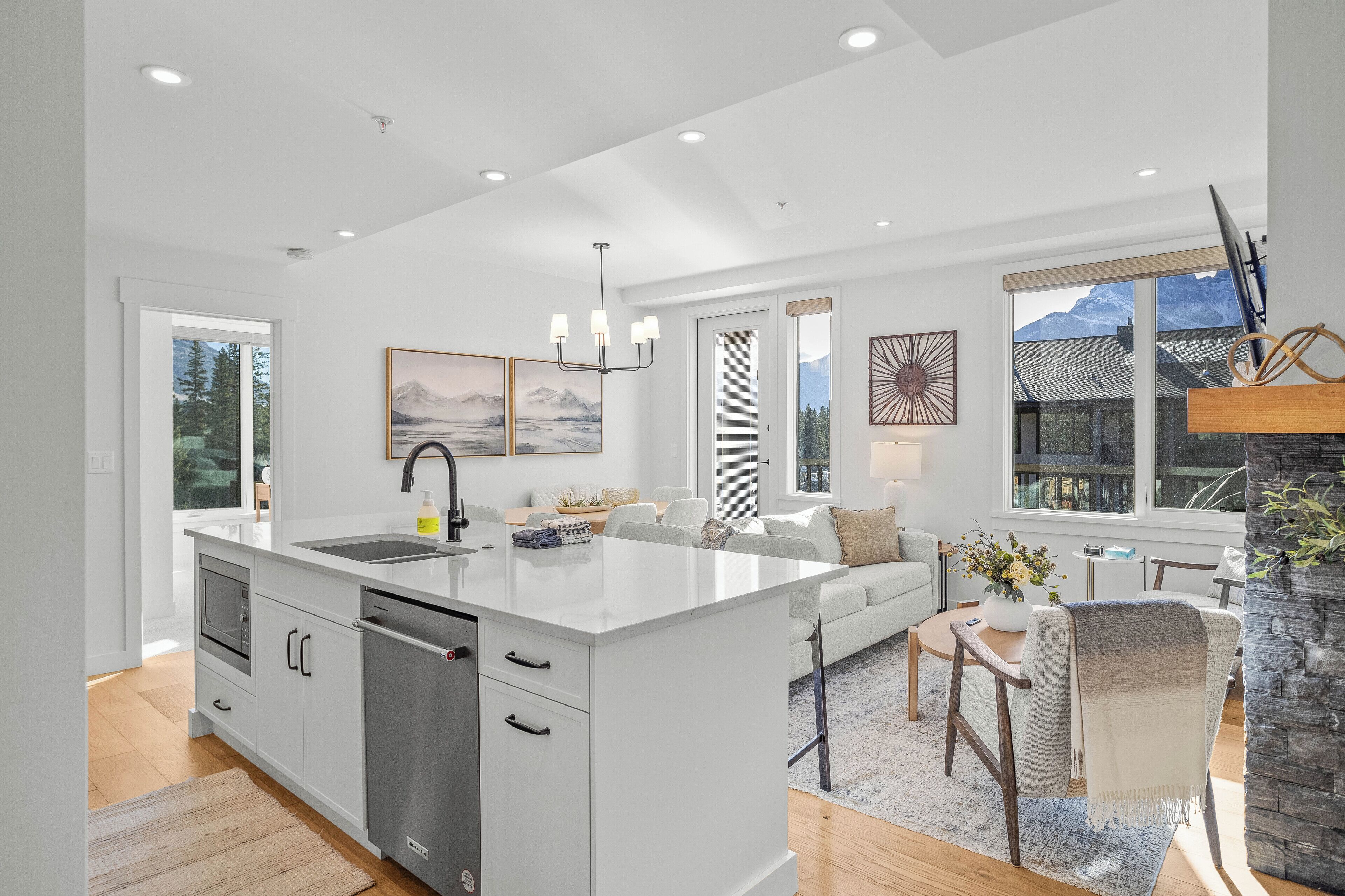 A modern kitchen with a large island, white cabinetry, and a stone fireplace.