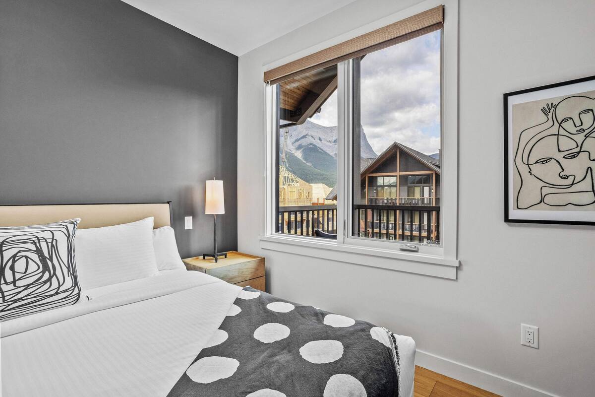 A bedroom with a large bed, a window with a mountain view, and a framed artwork on the wall.