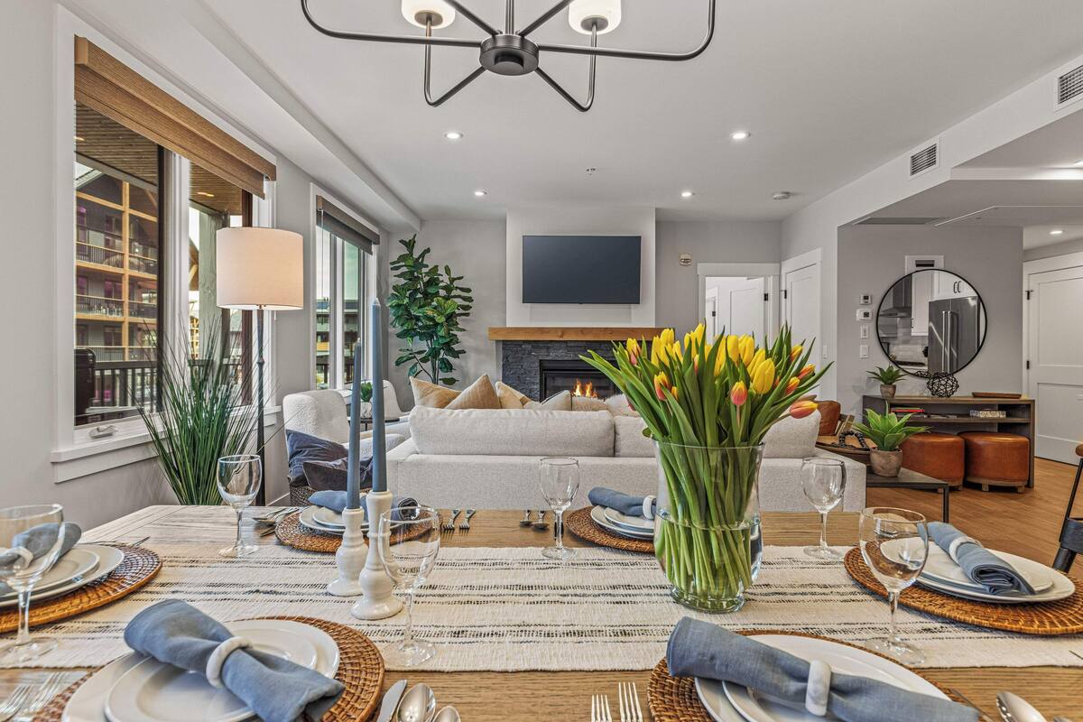 A dining area with a table set for four, a sofa in the background, and a fireplace.