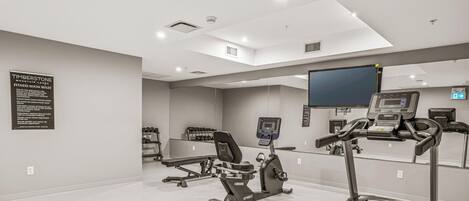 A modern fitness room with a treadmill, stationary bike, and weight bench.