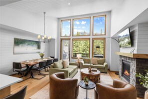 Un salon moderne doté d’une cheminée, de grandes fenêtres, d’un coin repas et d’un espace salon confortable.