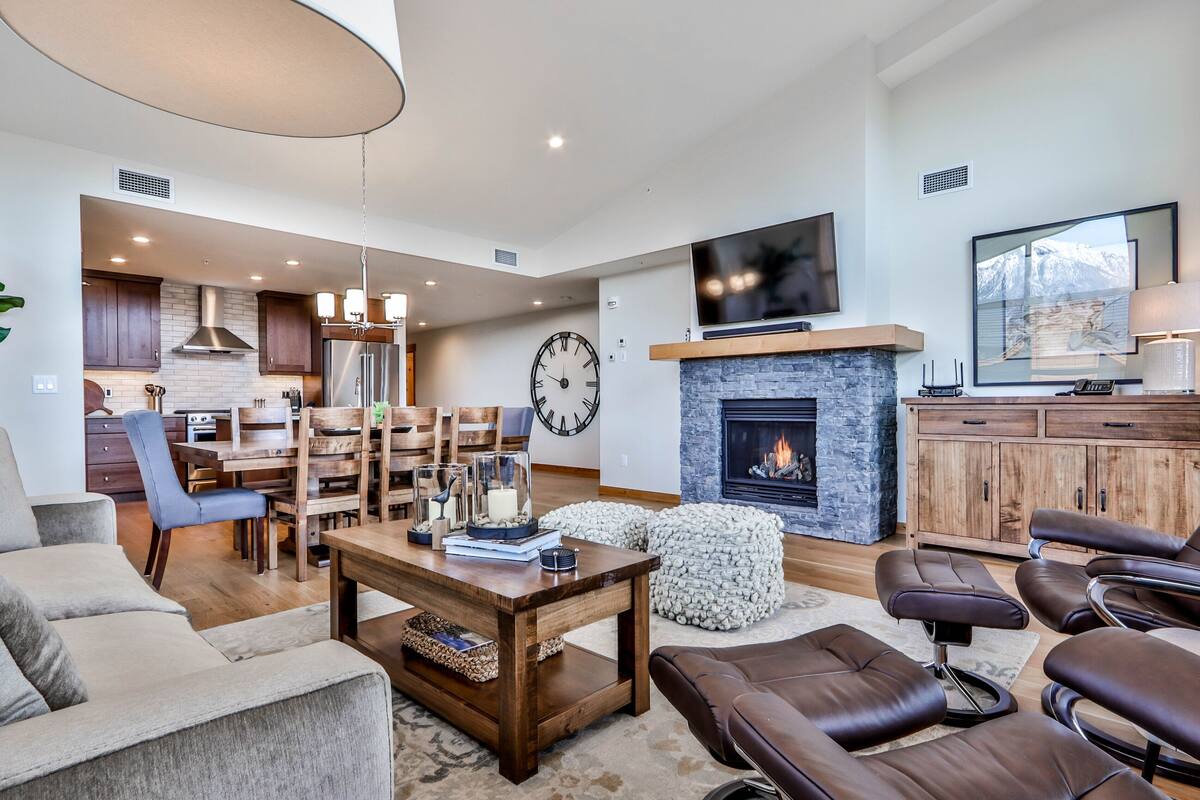 Una sala de estar moderna con chimenea, sofás de cuero, una zona de comedor y una cocina al fondo.