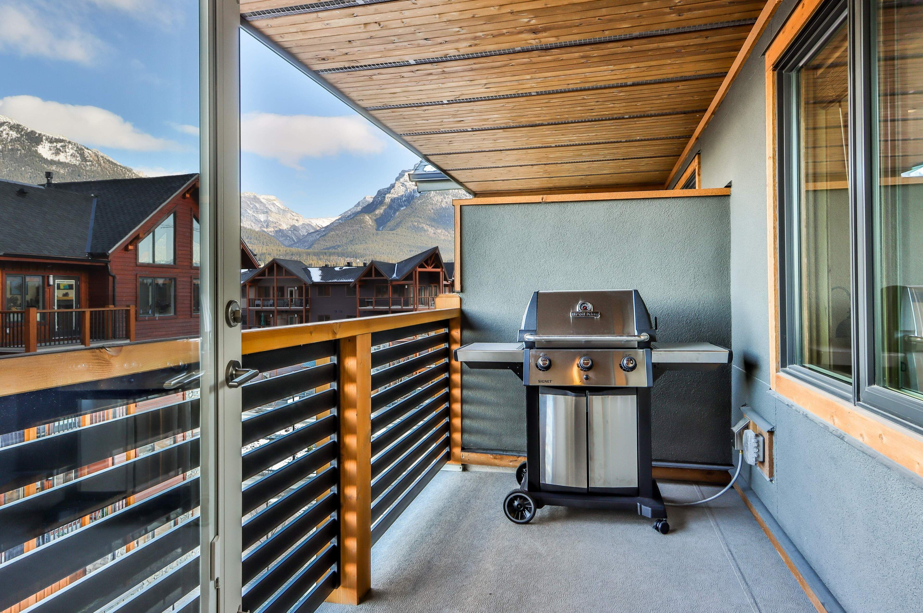 A balcony with a barbecue grill, wooden railings, and a view of mountains.