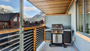 A balcony with a barbecue grill, wooden railings, and a view of mountains.