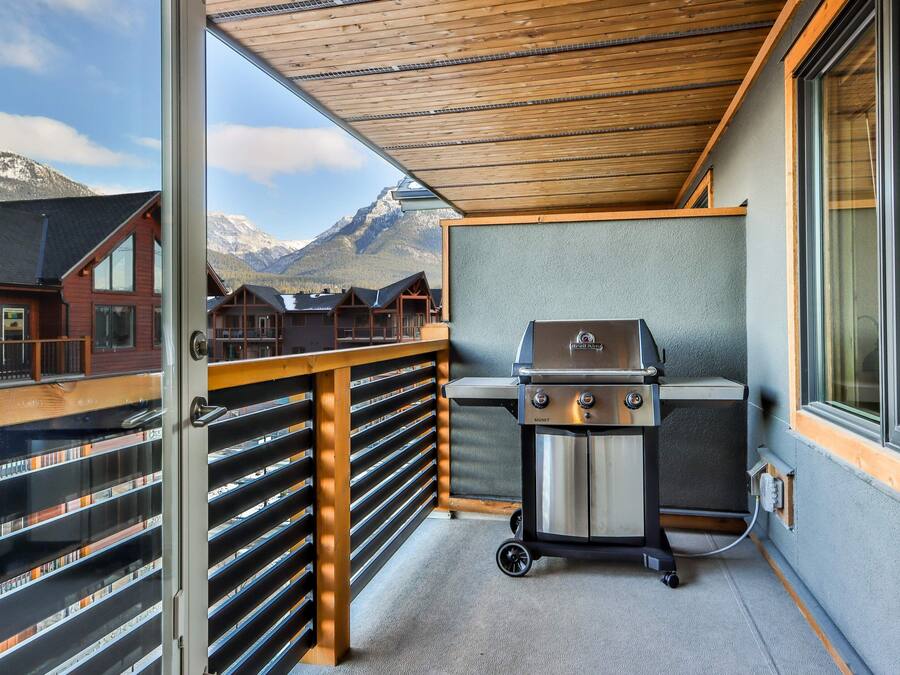 A balcony with a barbecue grill, wooden railings, and a view of mountains.