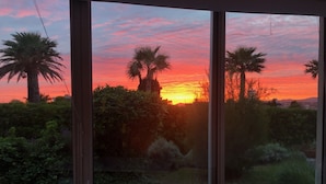 Huone, jossa on suuri ikkuna, josta avautuu näkymä puutarhaan auringonlaskun aikaan.
