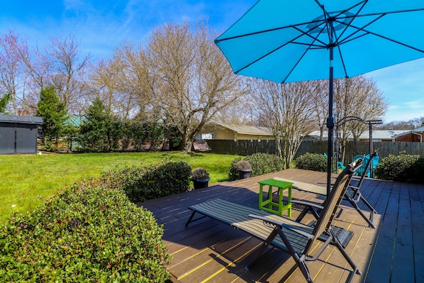 Une terrasse en bois avec un parasol bleu, une table verte et deux chaises longues.