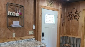 A kitchen with a granite countertop, a white door with a window, and a shelf with kitchenware. - Rustic studio country cabin w/shared pool, firepit, & outdoor kitchen (Lexington)
