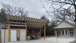 A rustic building with a covered patio area, a bar, and a small adjacent structure. - Rustic studio country cabin w/shared pool, firepit, & outdoor kitchen (Lexington)