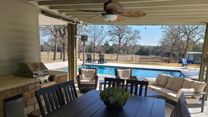 An outdoor patio with a grill, dining table, chairs, and a view of a swimming pool. - Rustic studio country cabin w/shared pool, firepit, & outdoor kitchen (Lexington)
