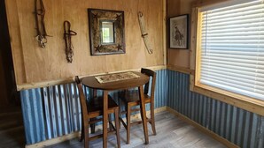 A wooden-paneled room with a table and chairs, a framed mirror, and a window with blinds. - Rustic studio country cabin w/shared pool, firepit, & outdoor kitchen (Lexington)