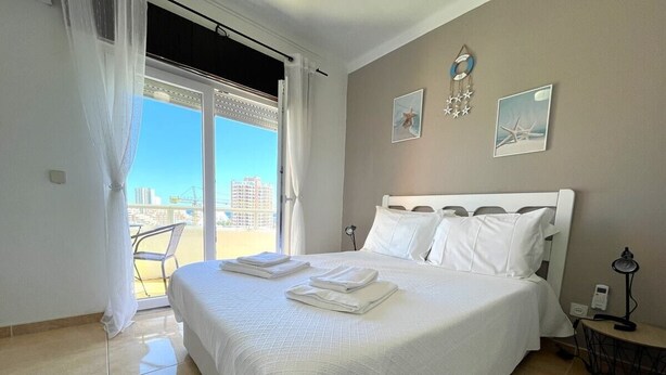 Ein Hotelzimmer mit einem großen Bett, einem Balkon mit Blick auf die Stadt und einem kleinen Tisch mit einer Lampe.