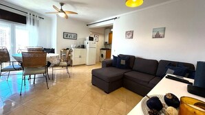 Ein modernes Wohnzimmer mit einer Eckcouch, einem Essbereich mit Korbstühlen, einer Küche im Hintergrund und einem Deckenventilator.