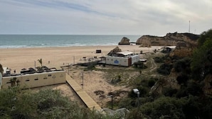 Ein Strand mit einem Felsen, sandigem Ufer und einigen Gebäuden, darunter ein weißes Gebäude mit einem blauen Schild.