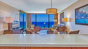 Habitación de hotel con una gran mesa de comedor, dos sofás, un televisor y vista al océano.